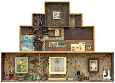 A three-tier sculpture mostly made of wood with various archival photographs, religious images, perfumes, and design elements.