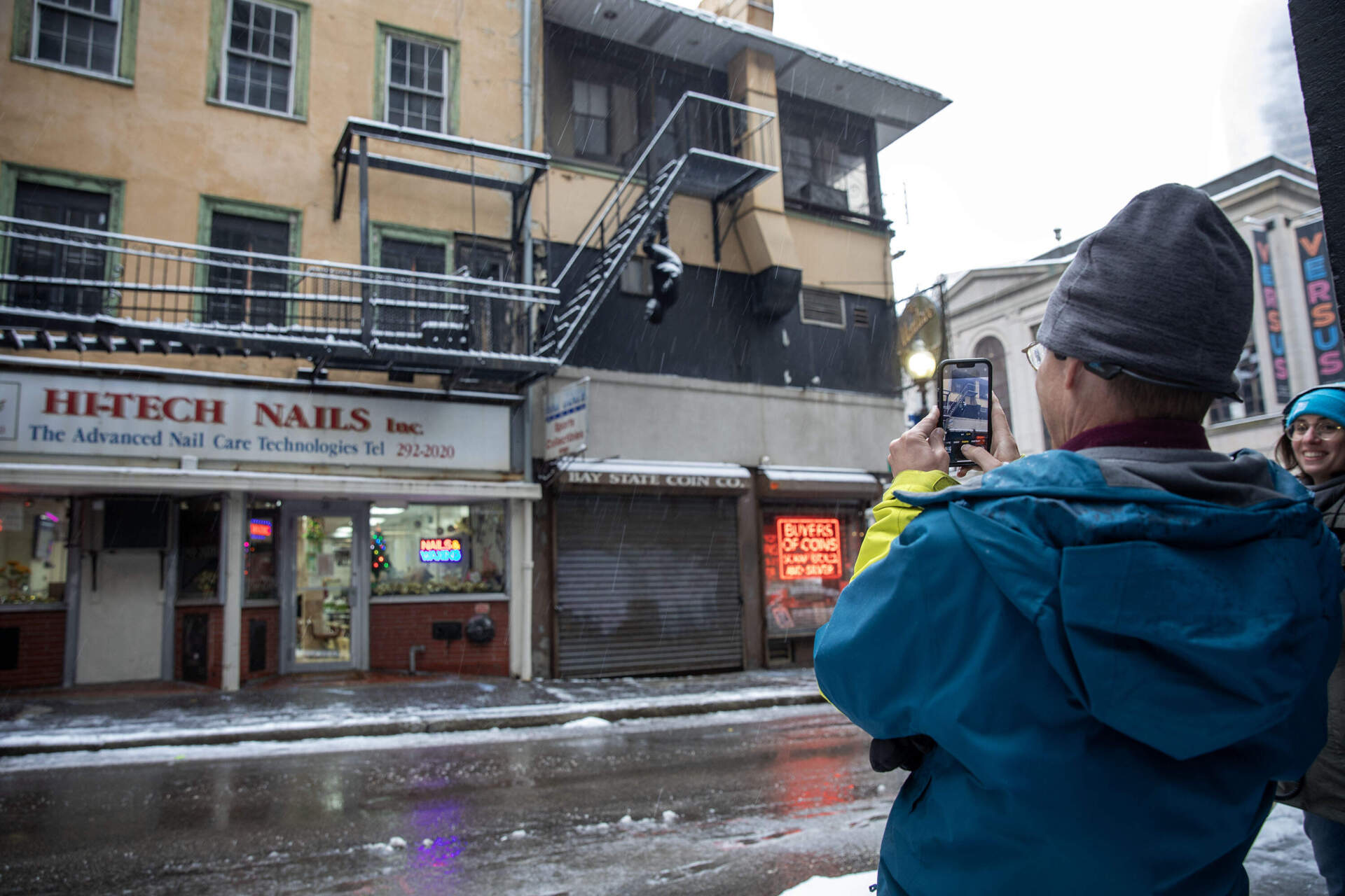 Mike McCart stops on Bromfield Street to take a photo of Mark Jenkins' untitled sculpture as it appears to walk down the underside of a fire escape. (Robin Lubbock/WBUR)