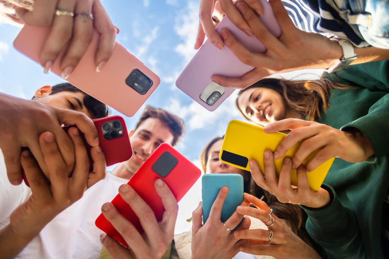 Young people standing in a circle using their cell phones.