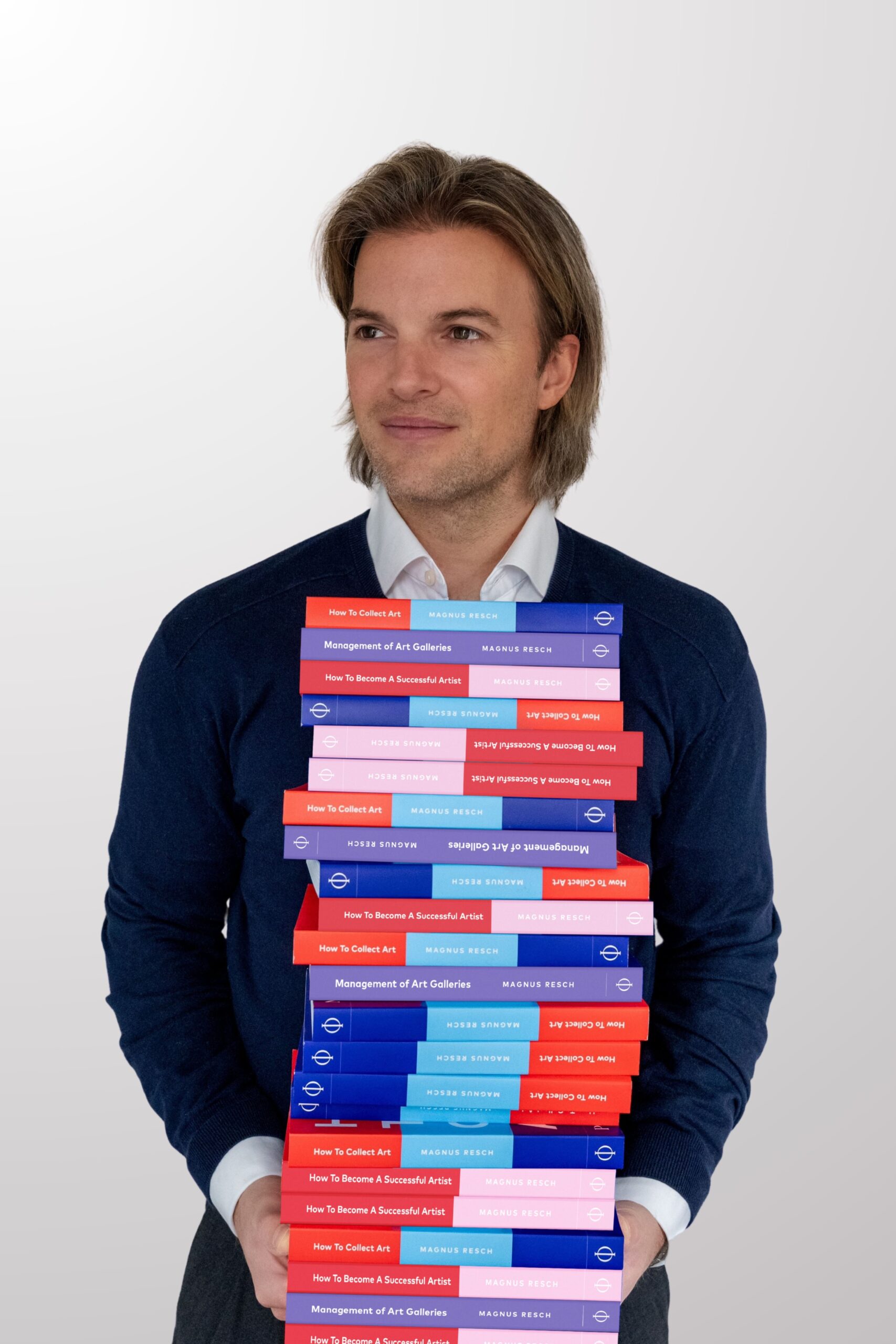 A man with longish hair holds a tall stack of colorful books