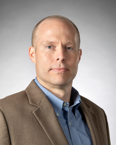 Man in blue dress shirt and brown suit jacket.