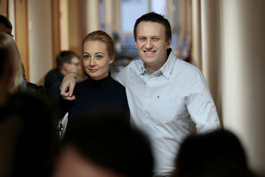 A woman and a man walk arm in arm down a hallway smiling.