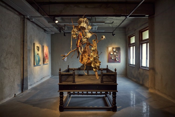 Pots and pans appear to defy gravity as they rise off a branch on a podium in a gallery