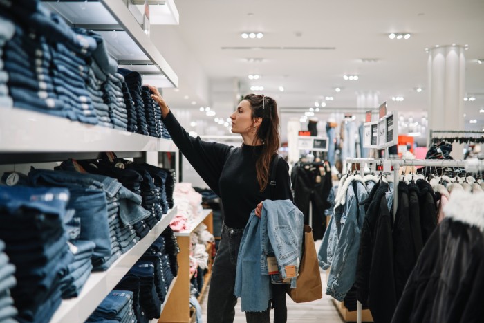 A woman browses through a shelf of jeans in a shop