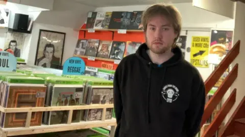 Jimmy Broklesby Jimmy Broklesby stood in front of a records shop in Frome in Somerset. There are various CDs and vinyl records, from different genre's including hip hop, reggae and soul.