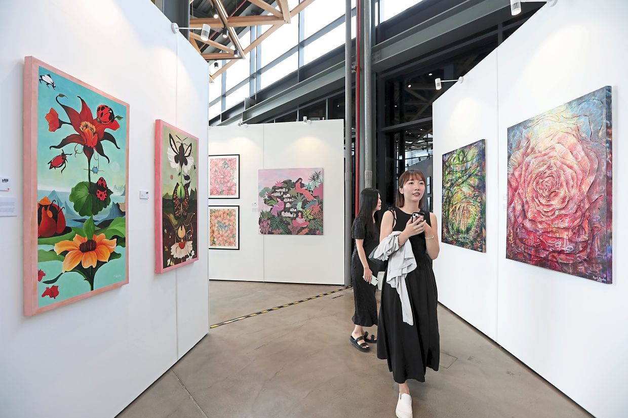 Visitors exploring the exhibition. On the left are Nana Ibrahim's paintings: 'Gila Atas' and 'Gila Bawah', while on the right are paintings from Syel Ramlan's  'Flowers Of Heaven' series. Photo: The Star/Yap Chee Hong