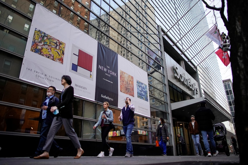 People walk past a non-descript building in a city with the word Sotheby's on its facade.