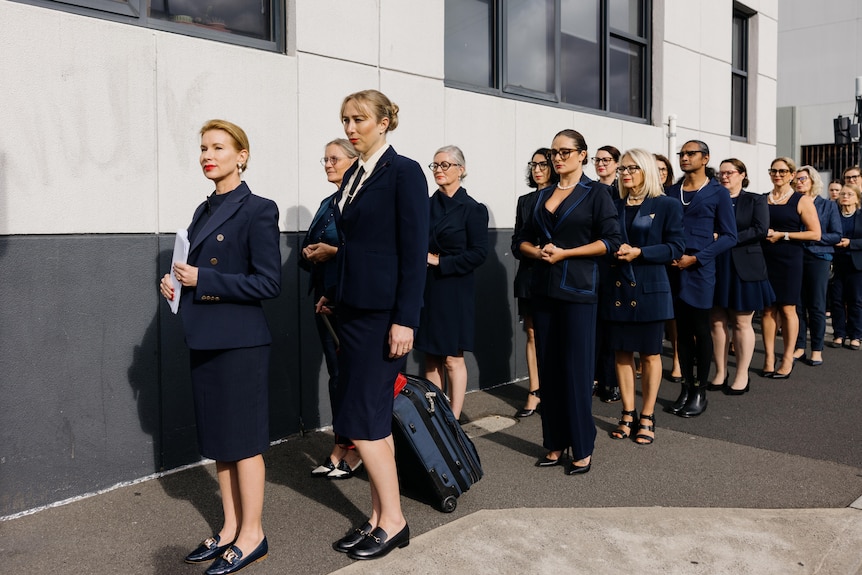 Women dressed in blue line up outside a building