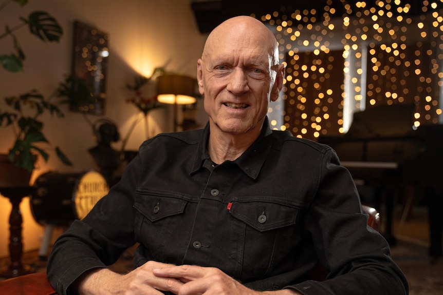 Peter Garrett sitting in a dark room lit by fairy lights with plants in the background.