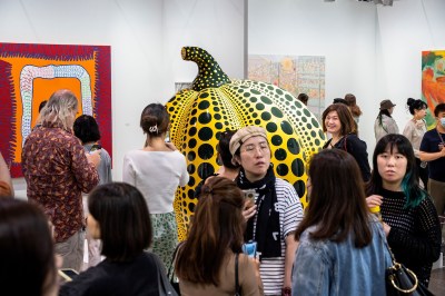 A group of people before a sculpture of a giant pumpkin with black dots on its yellow surface.