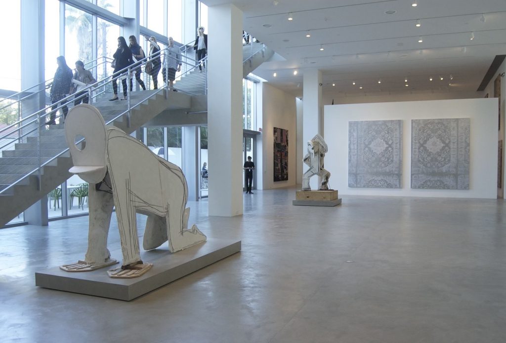 In a color photo, people descend a staircase in a tall and airy space. Two sculptures of abstracted people sit on low plinths.