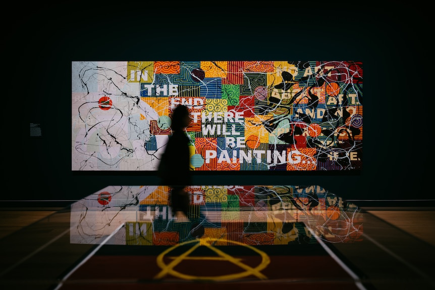 Darkened gallery shot, with large colourful painting on wall, featuring the text: IN THE END THERE WILL BE PAINTING.