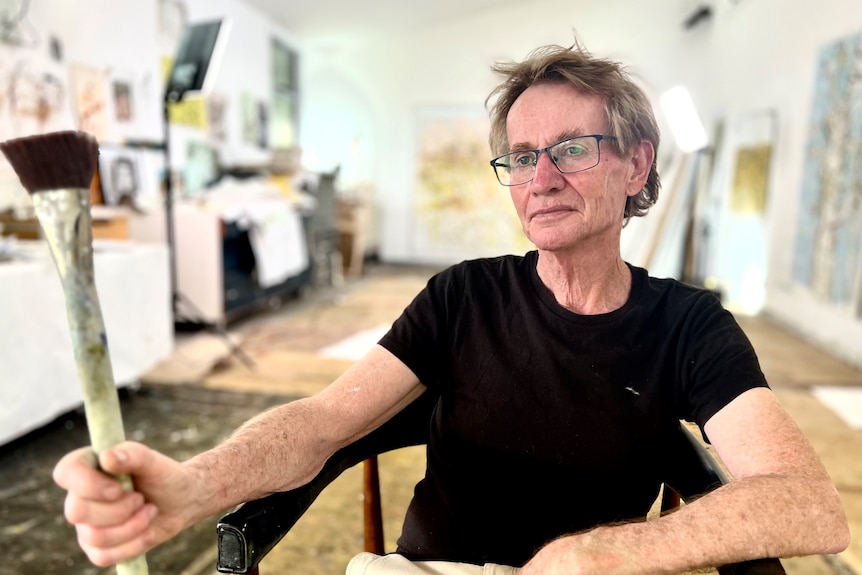 a man with big floor canvas and a paintbrush