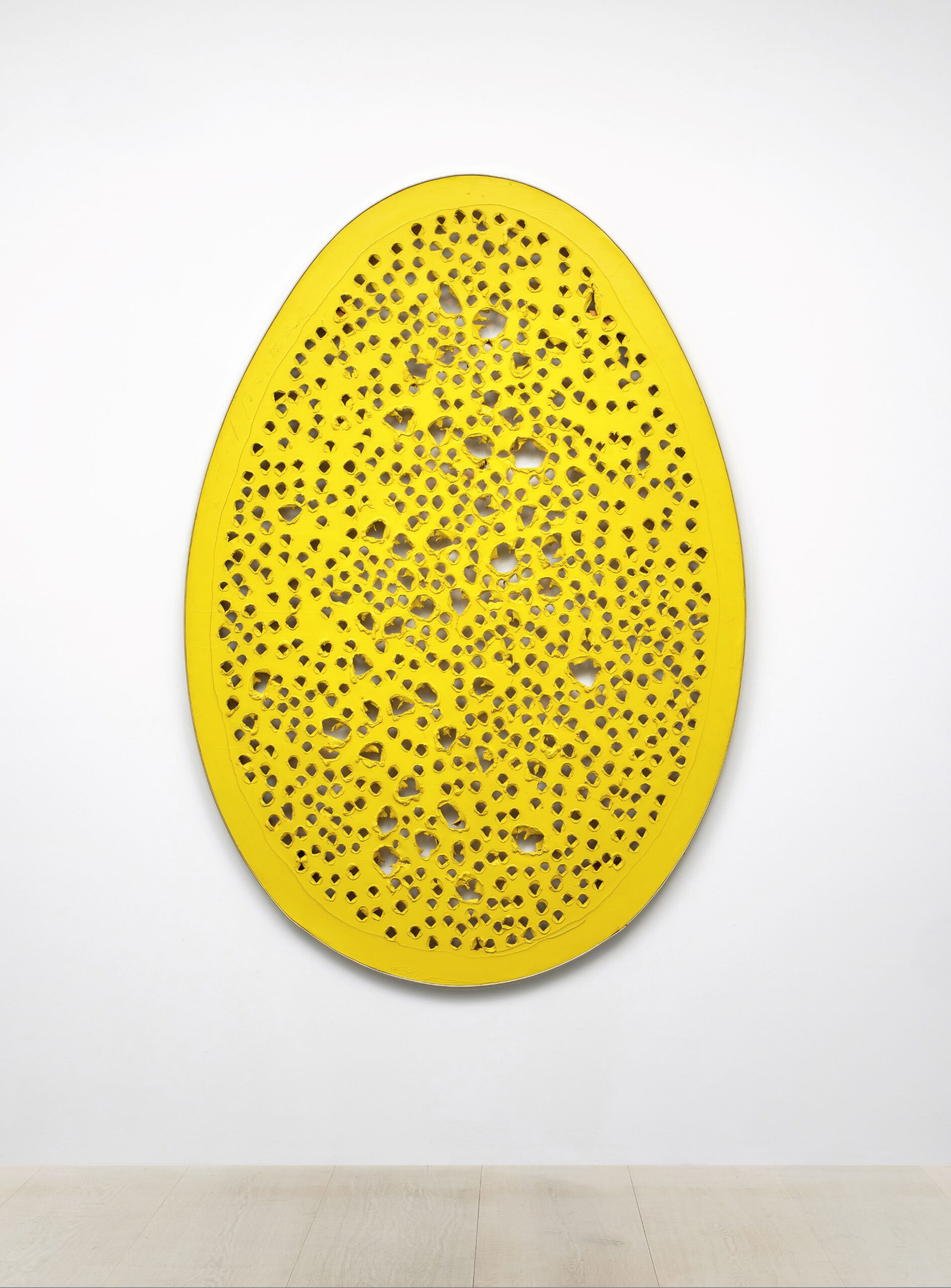 Yellow egg-shaped and perforated painting hanging on white gallery wall