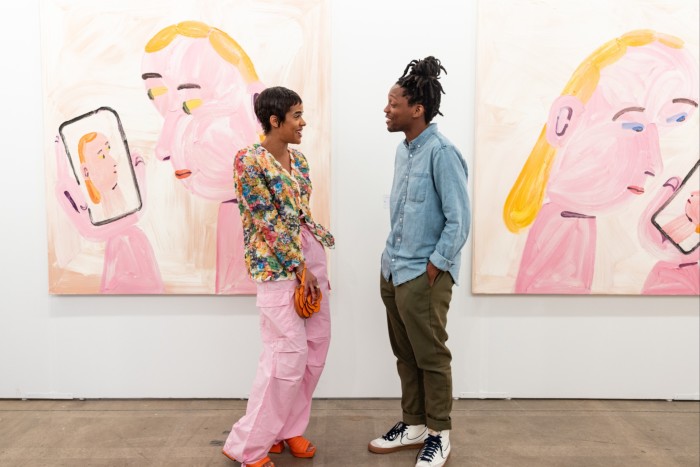 Man and woman chatting in an art gallery in front of two paintings of a person holding a mobile phone