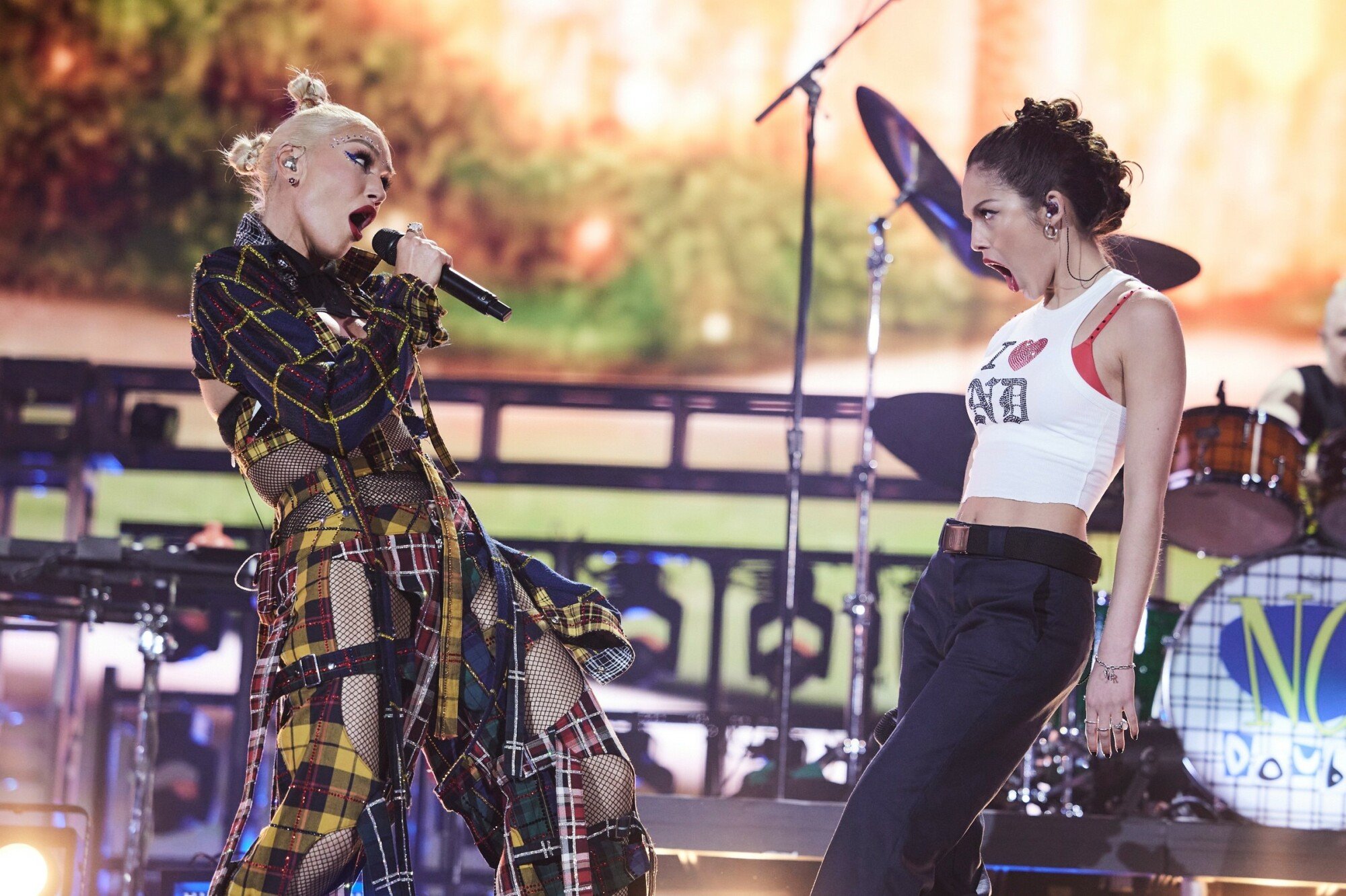 Stefani and Rodrigo onstage, facing each other. Stefani sings into a mic while Rodrigo opens her mouth in a look of surprise or awe.