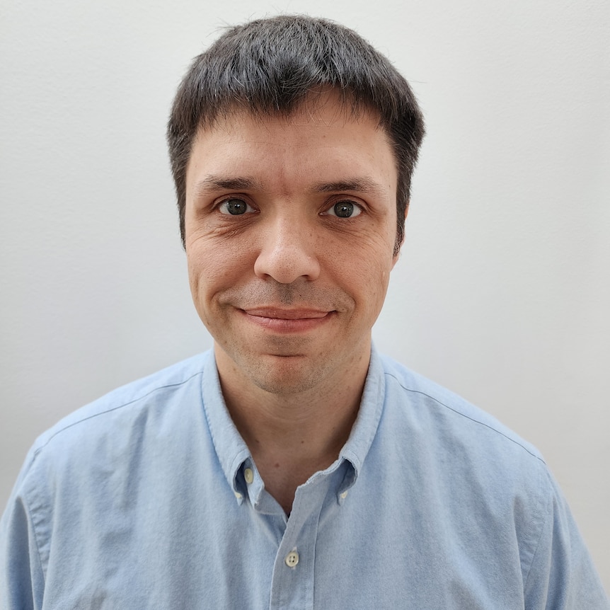 A close up portrait of a smiling, middle-aged man wearing a light blue collared shirt.