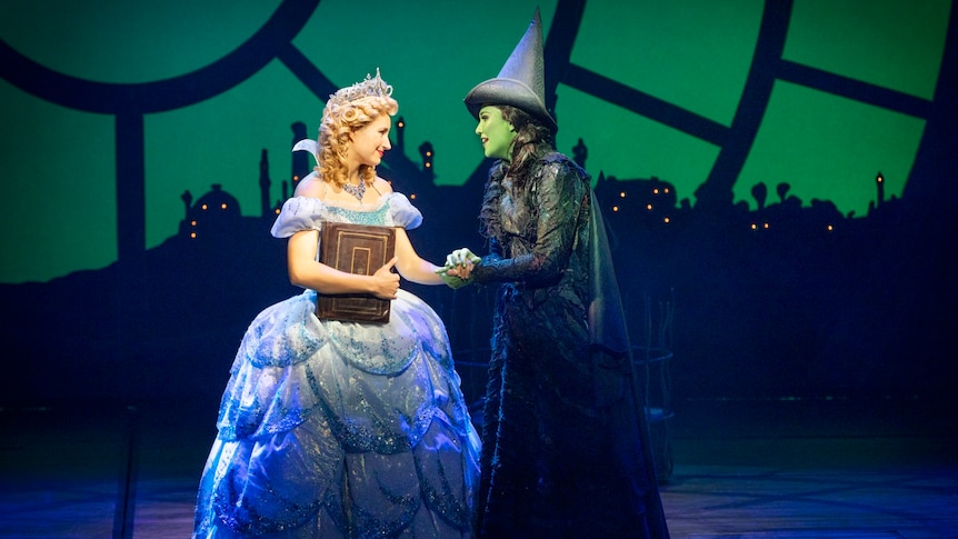 Courtney Monsma and Sheridan Adams as Glinda and Elphaba. Courtney is in a blue gown and Sheridan is in a black witch costume.