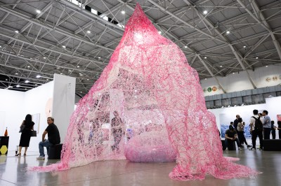 A large pink sculpture of yarn stands in the center of an art fair. 