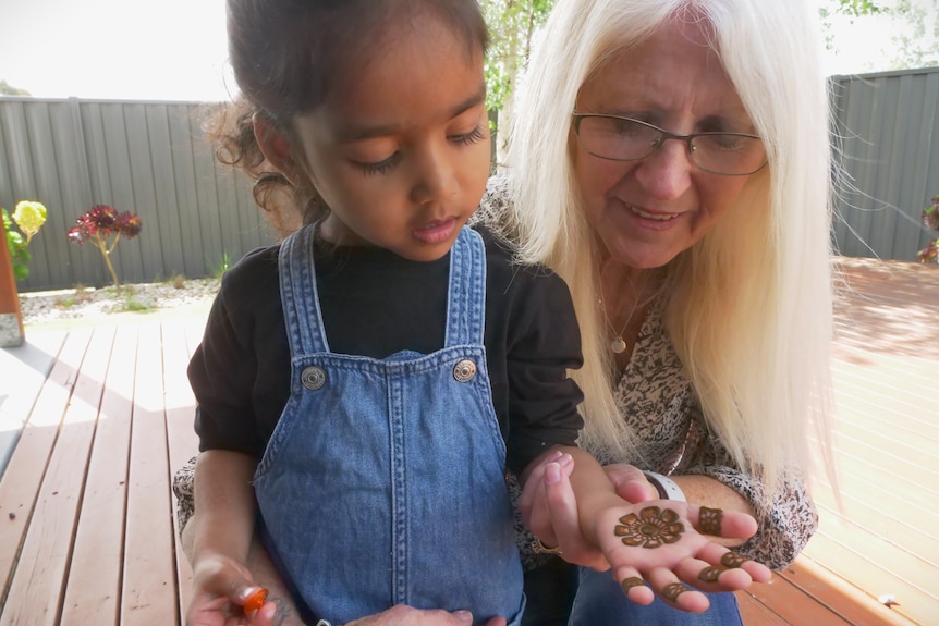 A young girl showing a small henna design on her hand to an older woman.