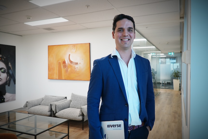 Peter Violaris stands with a laptop in hand in an office space