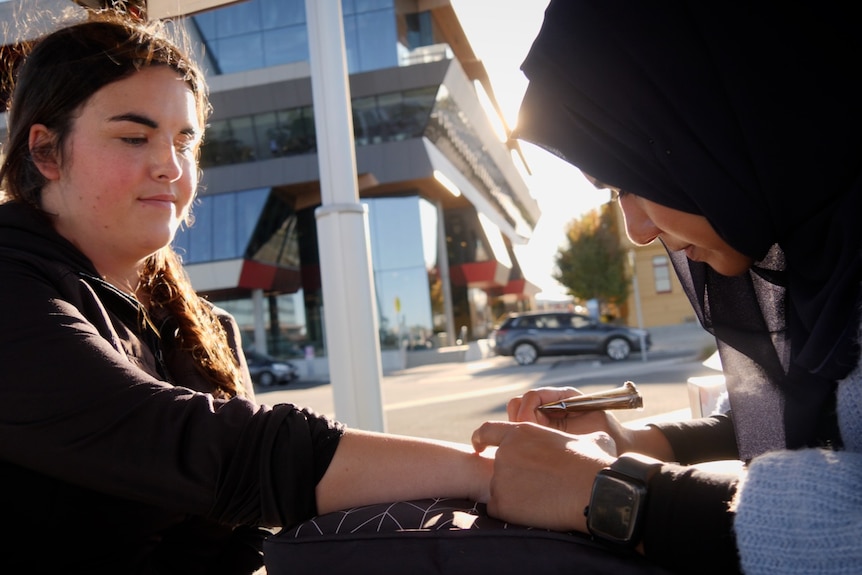 A woman holding her arm out as she gets a henna tattoo done by a henna artist