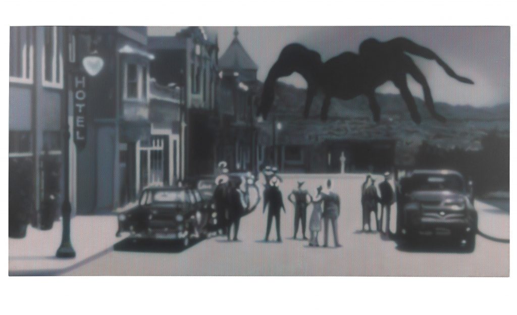 A black and white photo that looks like an old film still with people gathered in an old-timey downtown next to a vintage car looking at a massive tarantula approaching, one of the liaison's picks.