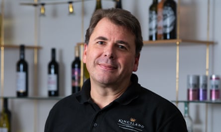 Ed Baker poses for a photo in front of shelves with wine bottles of them