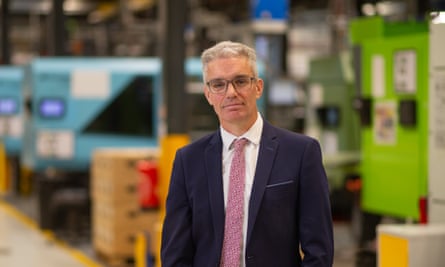 Kevin McNamee poses for a photo in a factory with machinery painted blues and greens out of focus int he background