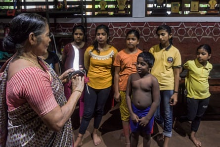 An older woman wearing a sari speaks to a small group of children and young teenagers.