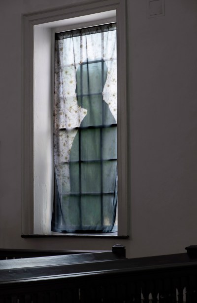 A floral sheet with a silhouette printed on it hangs in a window above the banister of a staircase. 