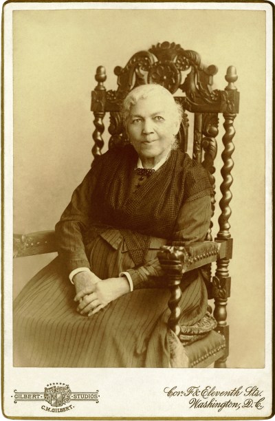 An archival portrait of Harriet Jacobs, an elderly Black woman seated in a wood-carved chair. 