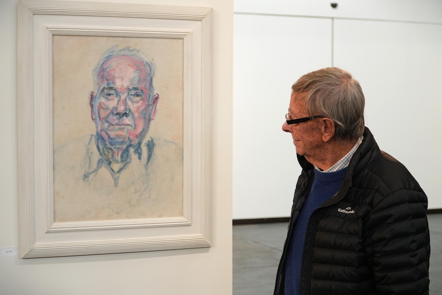 An older man named Bob Bunning stands in front of a portrait of a man.