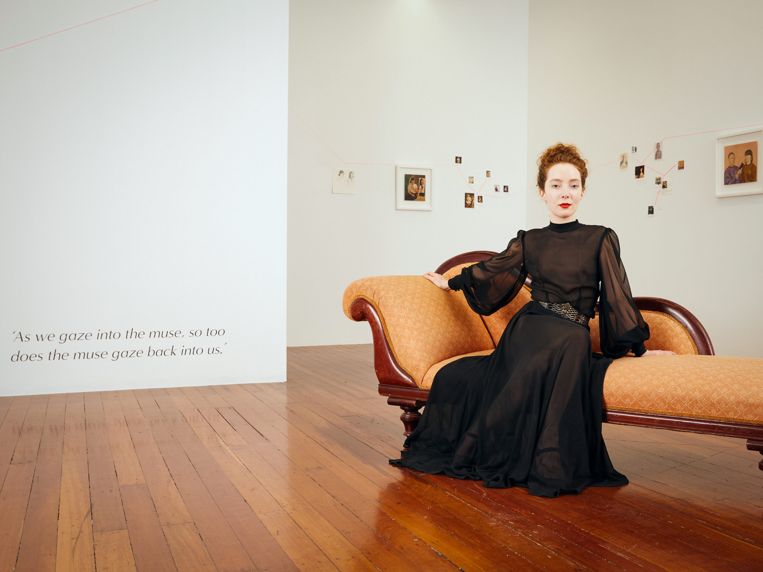 Artist sits elegant in her gallery in a black dress on a chaise lounge 