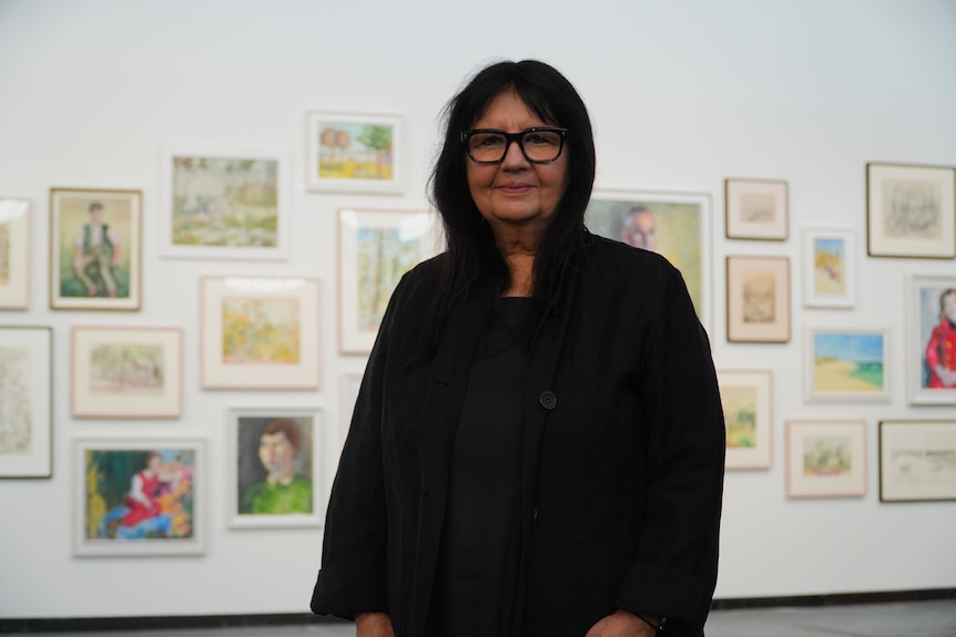 A woman in dark clothing smiles for the camera in an art gallery.