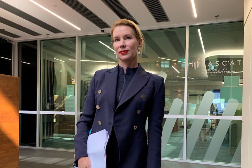 A woman wearing a navy blue suit looks sternly into the camera