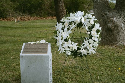 A wreath of white roses stands next to a placard for the Providence Burial ground. 