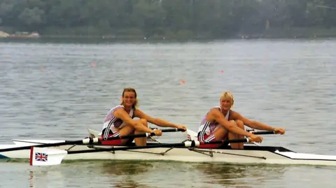 Maggie Phillips Annabel Eyres rowed and Alison Gill in a rowing boat on the water at the Barcelona Olympics. They are wearing red white and blue outfits and have British flags on their oars