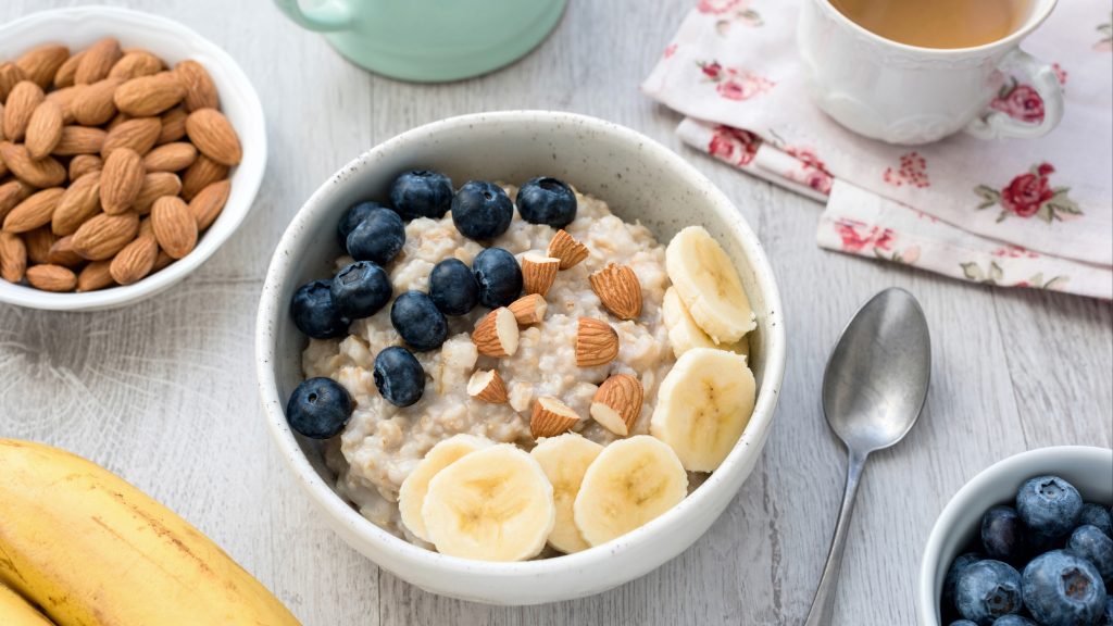 a healthy vegetarian breakfast of oatmeal porridge with banana, blueberries and nuts and cup of green tea