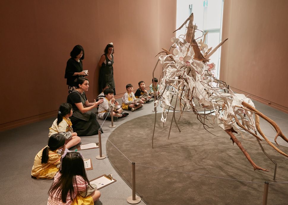 South korean kids drawing around a mostrous white scuplture made of sheels and wood. 