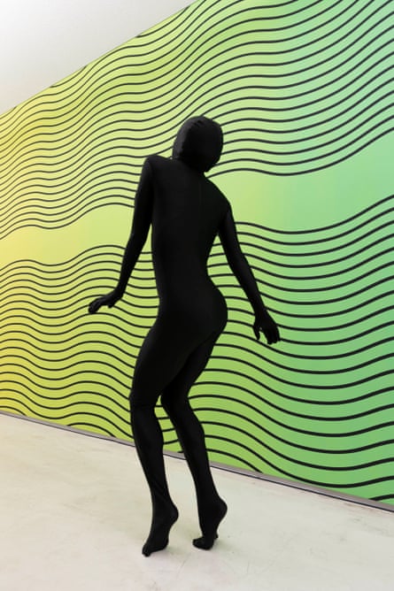 A woman on tiptoe, leaning down a bit to the right, is silhouetted against a wall of wavy lines