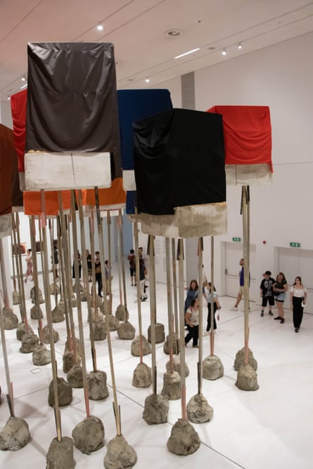 People walk through the artwork RIG: untitled; blocks (2011) by Phyllida Barlow, which consists of about 30 cement blocks covered in fabric and stuck on top of posts stuck in lumps