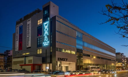 The EMST museum, with the neon sign What if Women Ruled the World, viewed at night from the front with lights from passing cars creating streaks