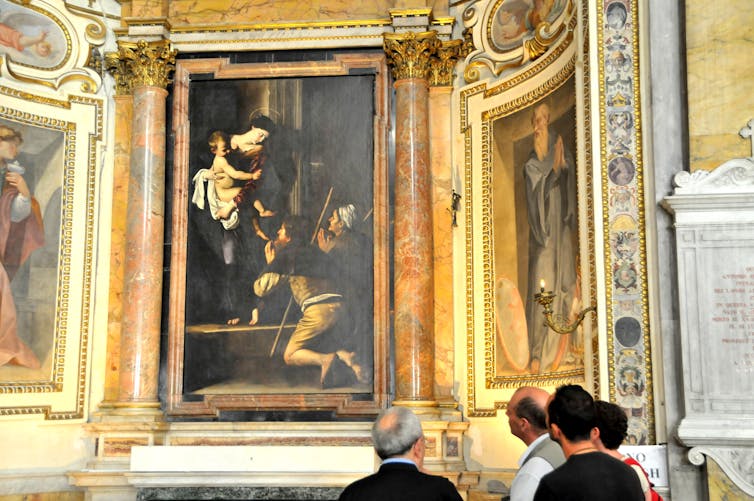 A woman, with a thin circular halo around her head, holds a child while two people kneel before her.