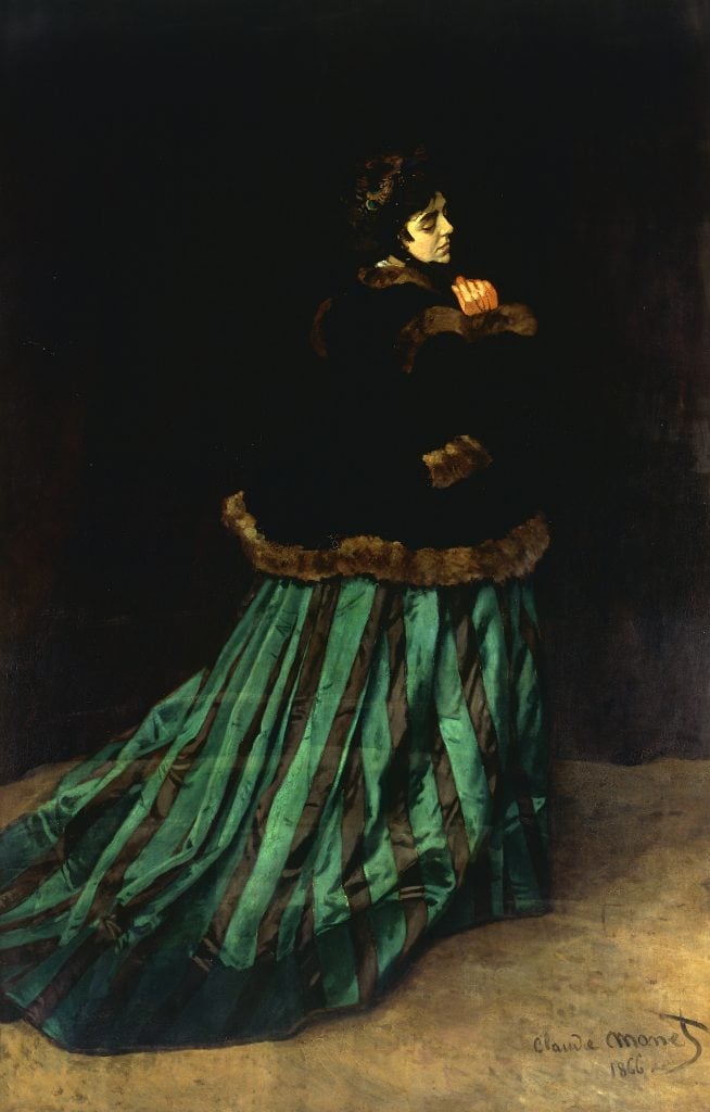 An image of a Monet painting featuring a woman in a long green dress with a black jacket facing away from the viewer but turning back slightly, on a brown floor and black background