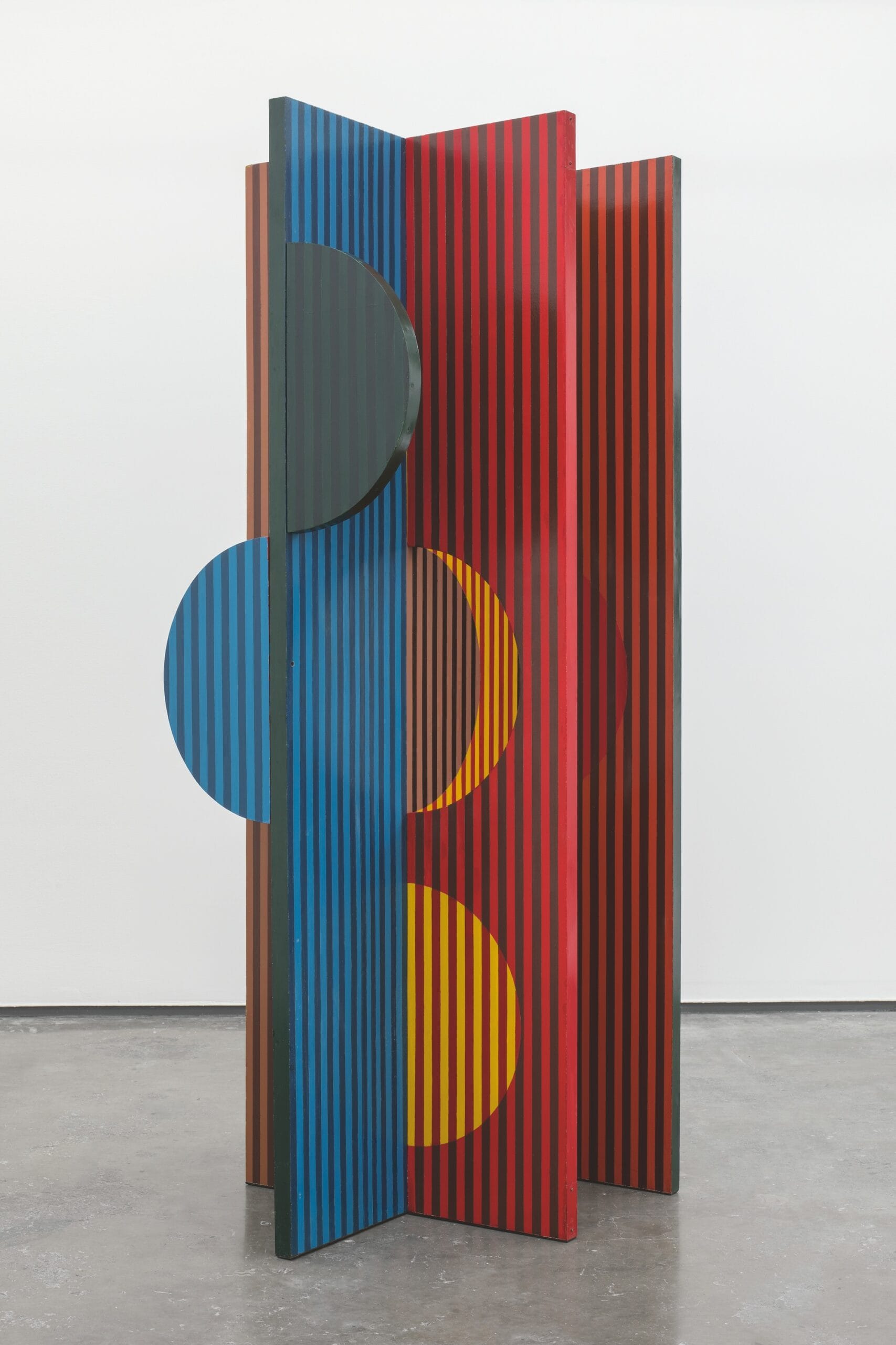 an abstract freestanding sculpture by Helen Escobedo featuring geometric facets and circular cutouts in black, red, blue, and yellow