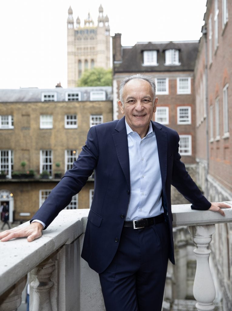 a man in a suit stands on a balcony. there are buildings and church spires behind him