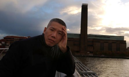 A man holds his head in his hand as he leans on the railing next to a river