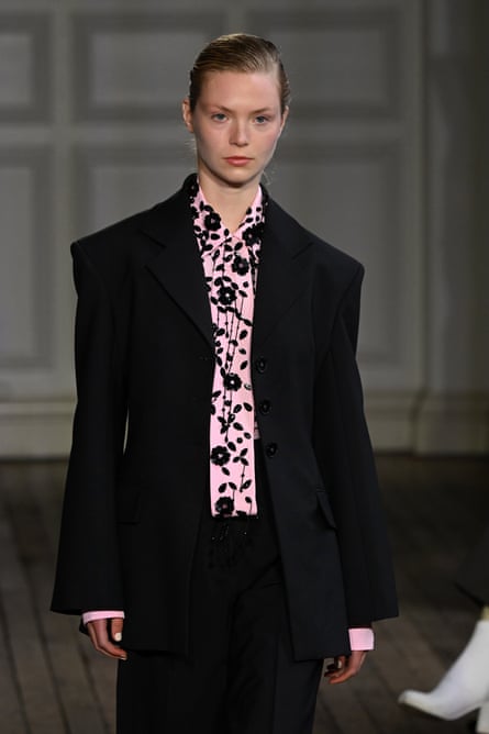 A model on the catwalk in a black suit with a pink and black shirt underneath