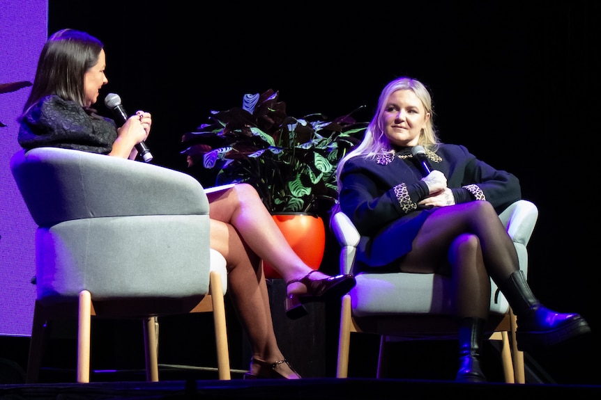 An image of Tones & I and Myf Warhurst at Bigsound sitting in chairs holding microphones 